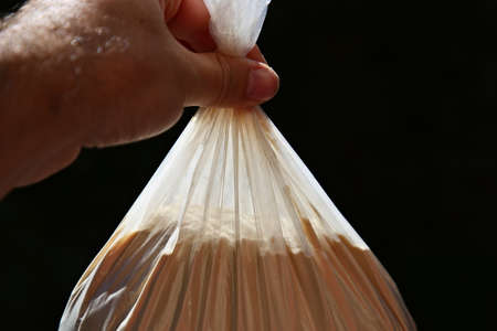 A closeup shot of a person holding a plastic bag full of flour with a black backgroundの写真素材