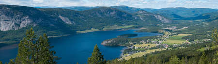 A panoramic shot of a lake surrounded by high rocky mountains under a cloudy sky