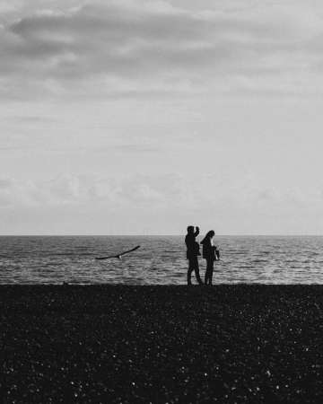 A man and a woman standing on the shoreline under a cloudy skyの写真素材