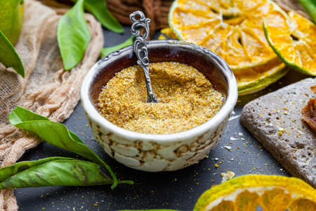 A closeup of tangerine powder in a bowl on a table surrounded by dry mandarines and leavesの写真素材