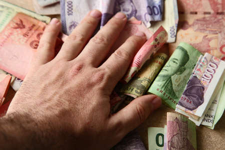 A high angle shot of a person holding banknotes from different countries on a wooden surface
