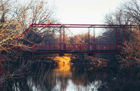 A bridge over a river in the middle of leafless trees under a cloudy sky