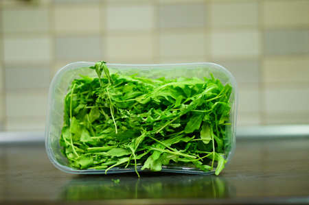 A closeup shot of arugula in a plastic bowl on a wooden surfaceの写真素材
