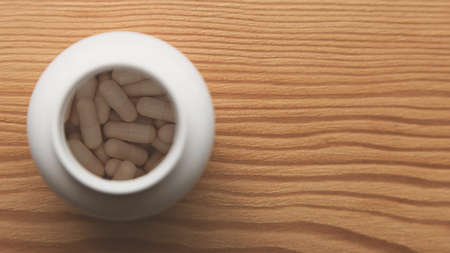 A high angle shot of capsules in a white container on a wooden surfaceの写真素材