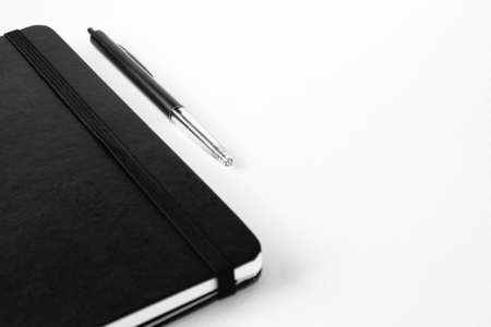 A selective focus shot of a pen near a notebook on a white surface