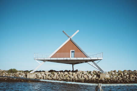 A shot of a triangle-shaped house in front of water under a blue sky