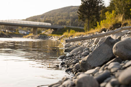 A closeup shot of a lot of rocks near the lake with a bridge in the background