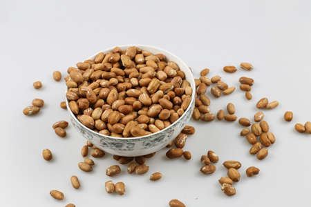 A high angle shot of a bowl of peanuts on a white surface