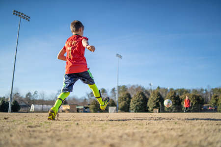 A closeup shot of a boy playing soccer in the field in a red uniformの写真素材