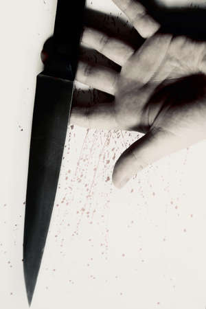 A vertical high angle shot of a hand holding a knife and drops of blood on a white surface