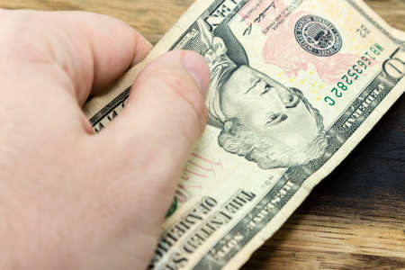 A high angle shot of a person holding a banknote over a wooden surface