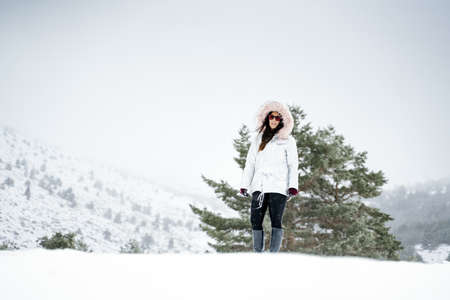 A wide shot of a woman wearing a white jacket standing on a snowy hill behind her on a winter dayの写真素材