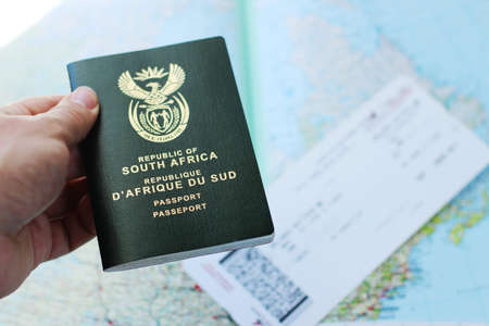 A high angle shot of a person holding a passport over a plane ticket and a geographical map