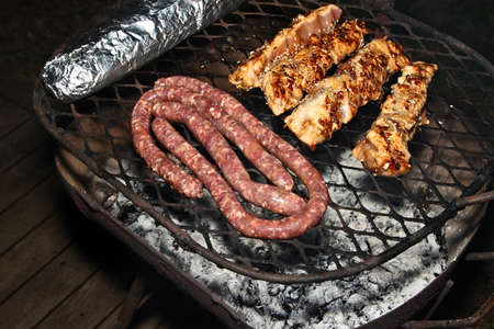 A high angle shot of some delicious meat  being cooked on a barbecue on a wooden porchの写真素材