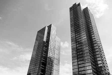 A low angle greyscale of modern skyscrapers with glass windows under sunlight