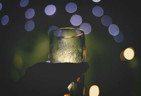 A selective focus shot of a person holding a glass with blurred lights in the backgroundの写真素材