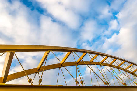 A low angle shot of a yellow cable-stayed bridge with a blue cloudy sky in the backgroundの写真素材