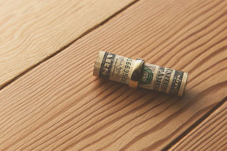 A high angle shot of dollar bills rolled in a golden ring on a wooden surface