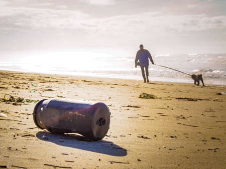 An old rusty barrel left on the beach with a person and a dog in the background - environmental...