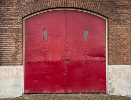 An arched type red metal door for a brick buildingの写真素材