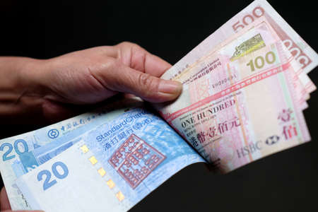 A closeup shot of a person holding Hong Kong dollars in front of a black background