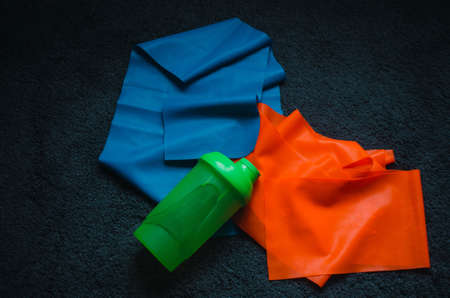 An overhead shot of a green water flask on a blue and orange rubber band