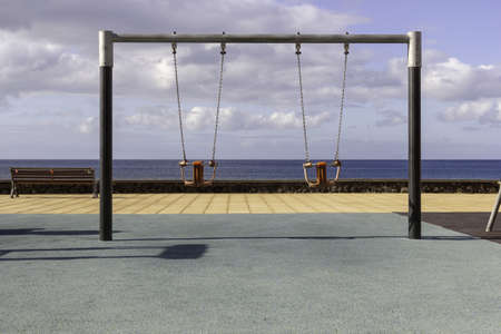 A roof with swings and benches surrounded by the sea under a cloudy skyの写真素材
