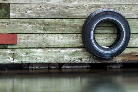 A black wheel of a car attached to a wooden wall above the waterの写真素材