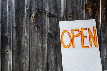 An open sign written in orange with a wooden fence in the backgroundの写真素材