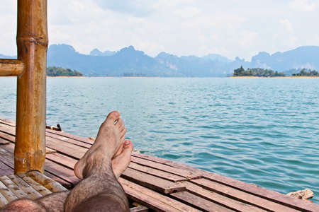 A person stretching his legs on a wooden pier over the beautiful calm oceanの写真素材