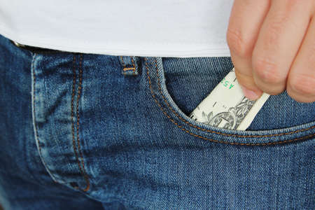 A closeup shot a person putting a dollar bill in the pocket of his jeans