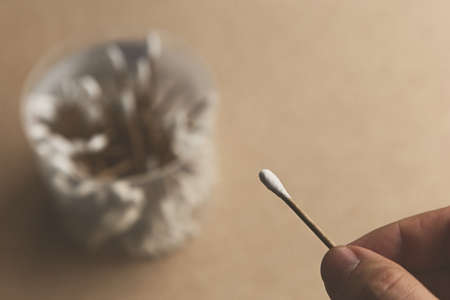 A closeup shot of a person holding a cotton swab over a package of cotton swabsの写真素材
