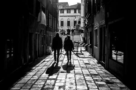 A grayscale shot of two men walking down an alley casting shadows on the foregroundの写真素材
