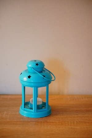A vertical shot of a blue lantern with a candle inside on a wooden surface