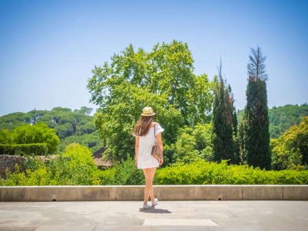 A young female in a white dress walking in a park enjoying the beautiful view of a green forest