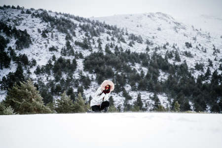 A wide shot of a woman kneeling down on a hill with trees on a snowy day
