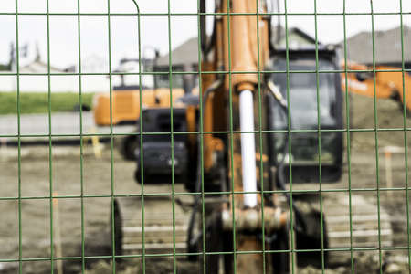 A closeup of chain-link fences with a construction truck in the dirt on the blurry backgroundの写真素材