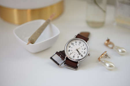 Stylish watch with leather band set at 4:20 with cannabis joint on sidetable with lamp, flowers, and...