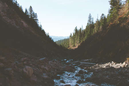 A river surrounded by hills and rocks covered in forests under the sunlightの写真素材