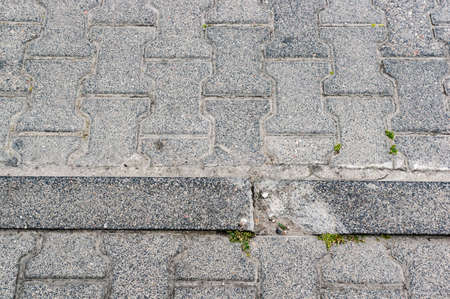 A closeup shot of the edge of a sidewalk with grey concrete tiles