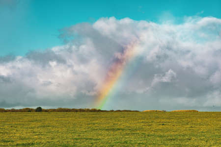 A beautiful shot of an empty grassy field with a rainbow in the distance under a blue cloudy sky in Englandの写真素材