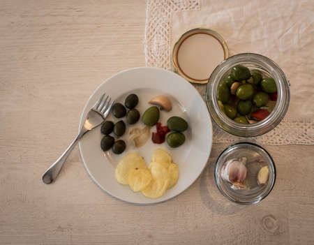 An overhead shot of a plate on a white table with green and black olives and a garlicの写真素材