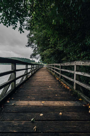 Wooden walkway or bridge on the side of a lake. Old wooden path on the bank of a lake. Autumn view of a wooden path and a lake.の写真素材