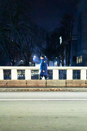 A vertical shot of two males walking through the sidewalk near the street at nightの写真素材