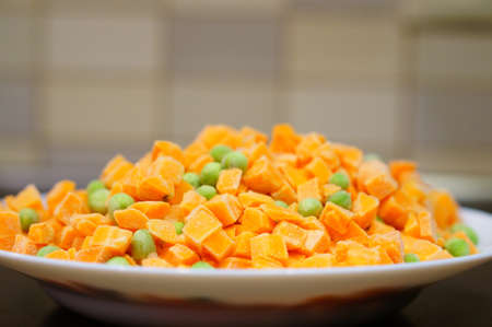 A closeup shot of sliced carrots and green peas in a white plateの写真素材