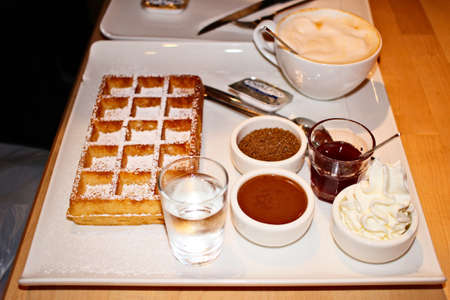 A high angle shot of a delicious waffle with a cup of cappuccino and other delicious desserts