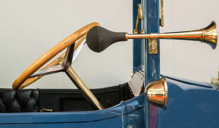 The front of a vintage blue car with an antique golden steering wheel and a separate hornの写真素材