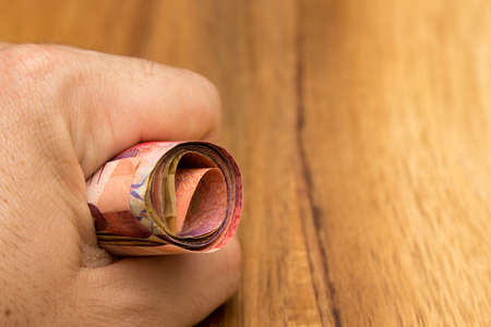 A high angle shot of a person holding a bunch of banknotes over a wooden surface