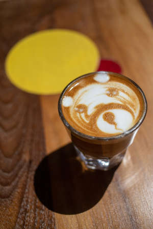 A vertical closeup shot of a coffee with milk on a wooden table with a bear image in itの写真素材