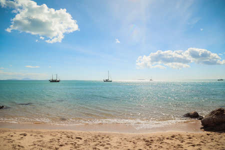 A beach surrounded by the sea with ships on it with the hills under sunlight on the background